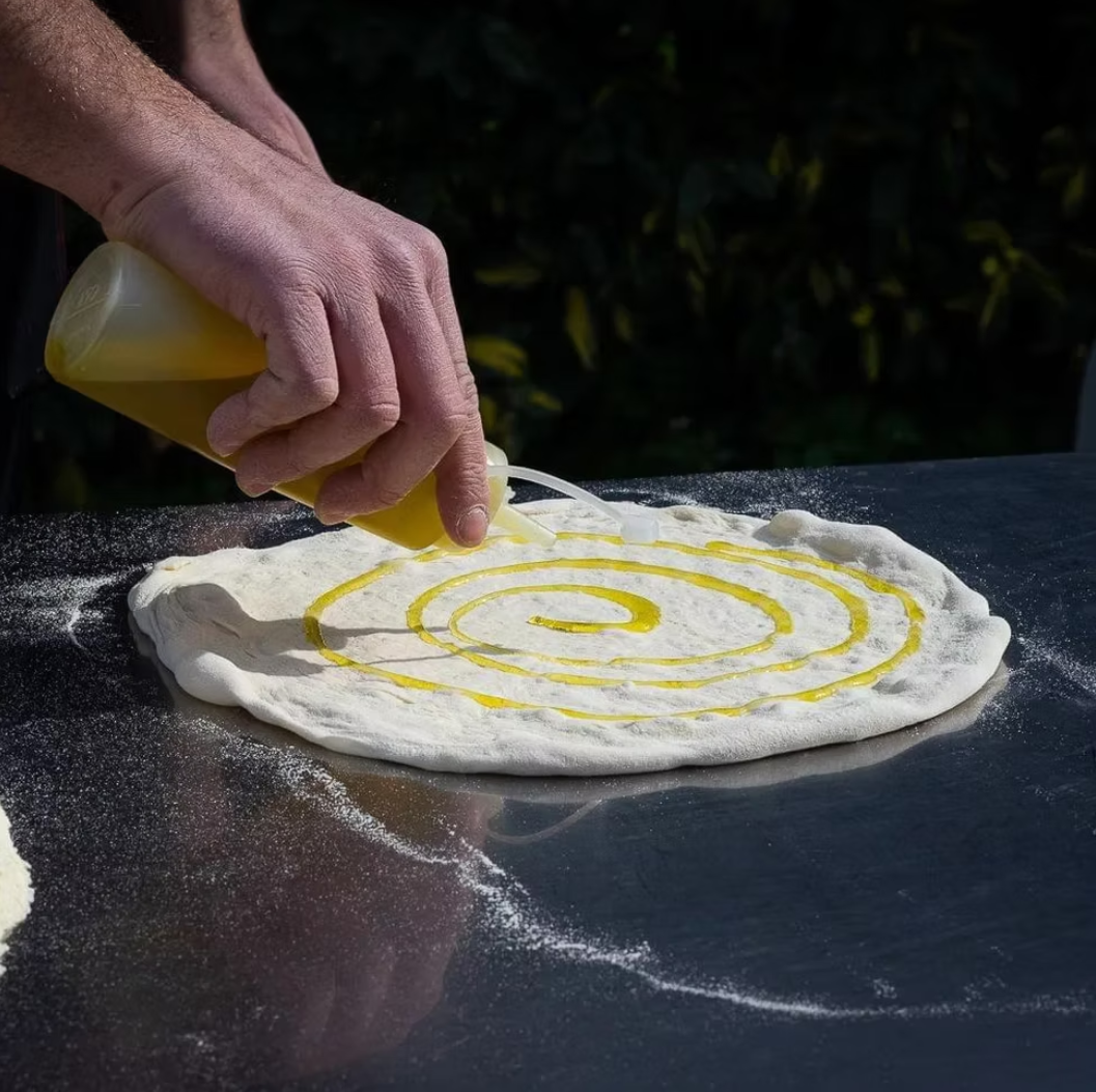 Chef Othman drizzling olive oil in a perfect spiral over fresh pizza dough