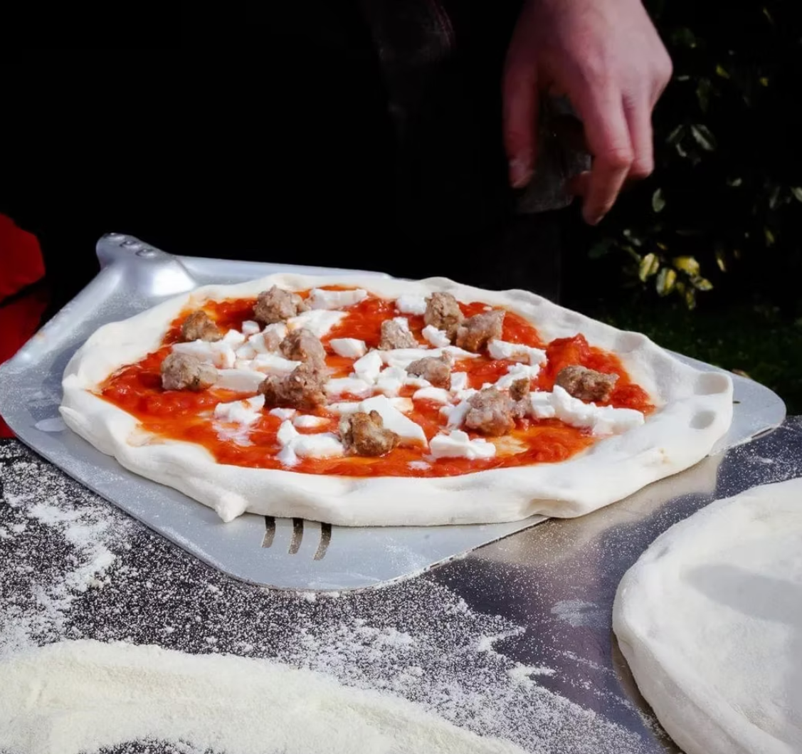 Pizza with sausage and mozzarella on a professional peel, ready for the oven